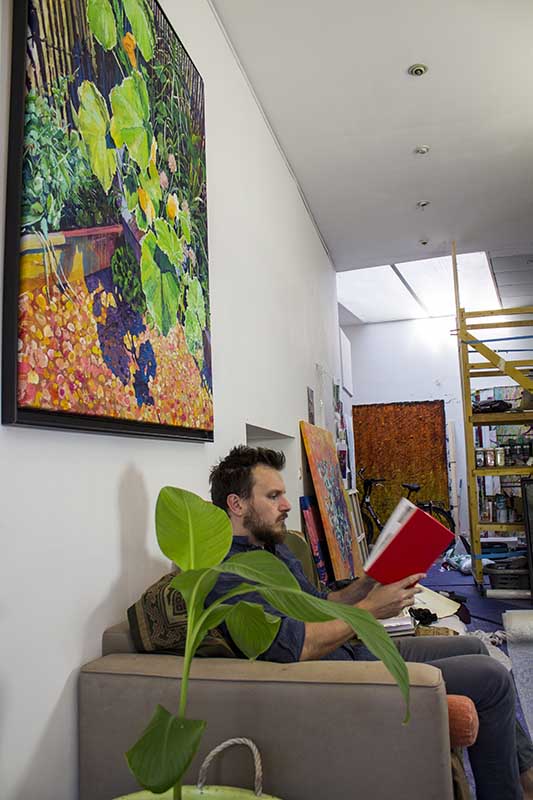 
Dominic Virtosu contemporary artist reading a book on the couch of his studio in front of the original framed artwork a quiet corner